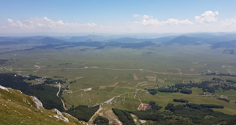 Paraglajder iznad širokog planinskog pejzaža